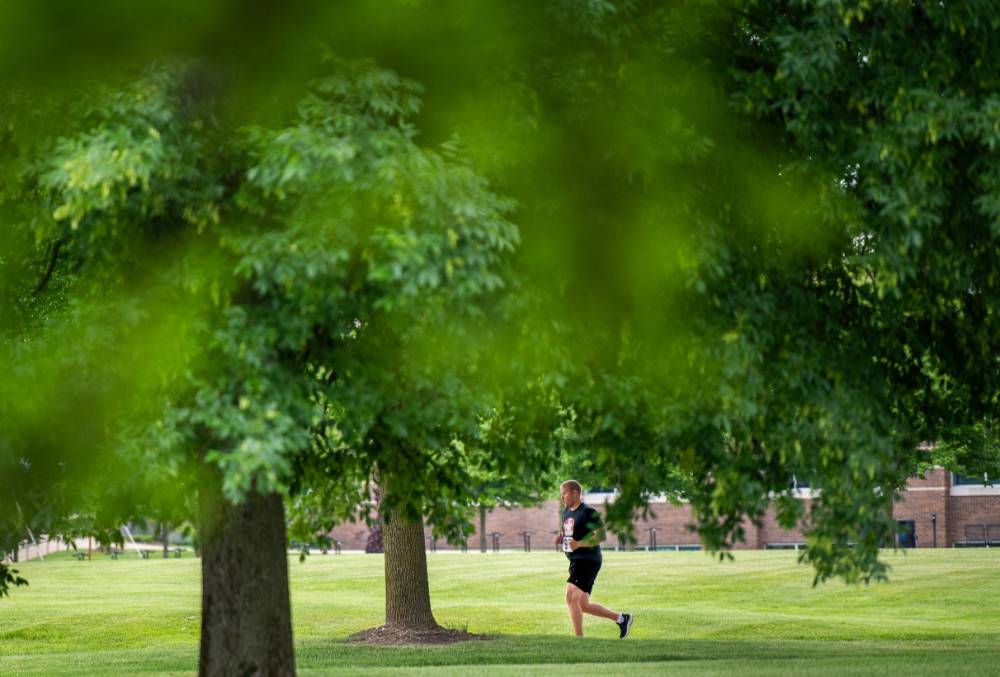 Man running under low-hanging trees on campus